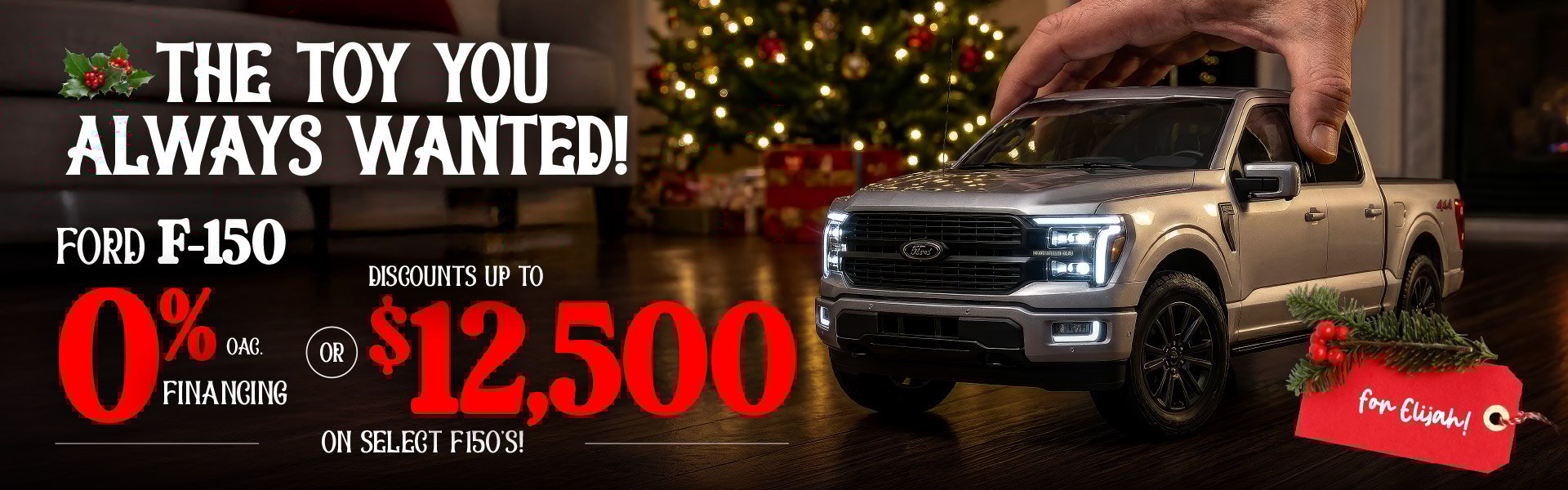 A hand positions a toy-like silver Ford F-150 on a hardwood floor in front of a sparkling Christmas tree. Bold holiday graphics highlight 0% financing OAC or up to twelve thousand five hundred dollars in discounts on select F-150 models, with a festive red tag reading “for Elijah!”